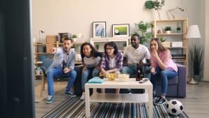 Diverse group of friends cheering for a sports game in a cozy living room setup.