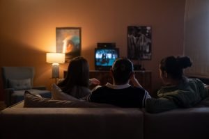 Three people enjoying a relaxed movie night at home, sitting on a couch in a cozy living room.